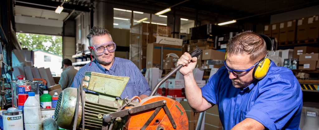 Twee mannen aan het werk achter een machine in een werkplaats